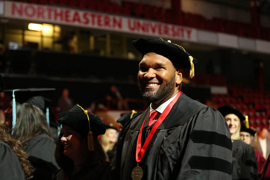 CPS doctoral graduate smiles while entering Matthews Arena at the 2022 May CPS Doctoral Hooding Ceremony