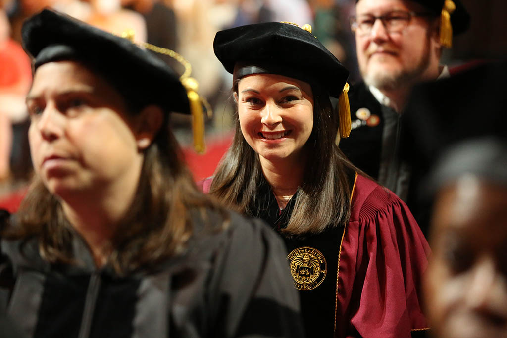 Female doctoral graduate smiles at camera while sitting among other graduates during the May 2022 CPS Doctoral Hooding Ceremony