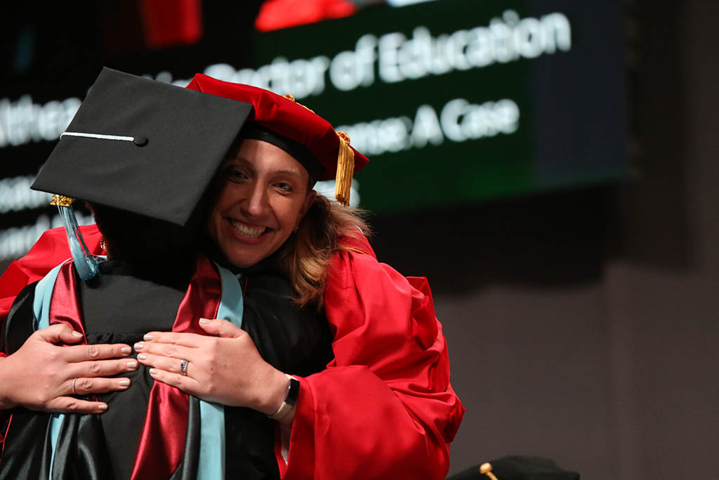 Faculty adviser hugs doctoral graduate on stage at the May 2022 CPS Doctoral Hooding Ceremony
