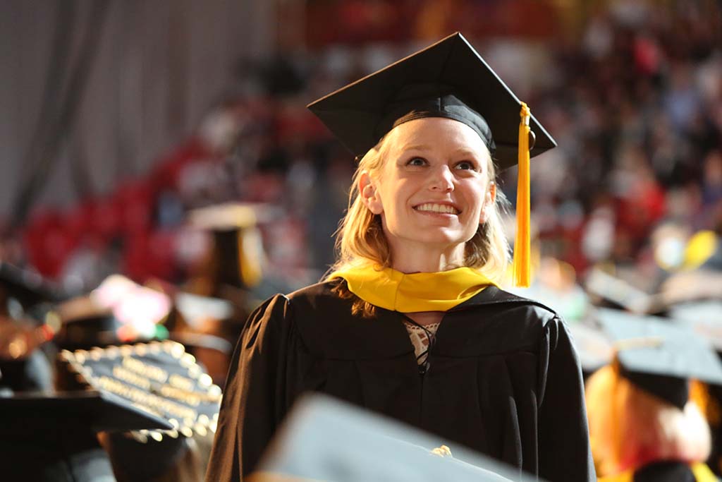A female CPS graduate smiles and looks up from the audience at the 2022 May CPS Graduation Ceremony in Matthews Arena. Photo by Heratch Ekmekijan