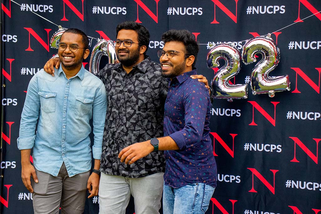Three diverse male CPS graduates pose for the camera in front of 2022 NU CPS celebration photo backdrop. Photo by Denise Reid