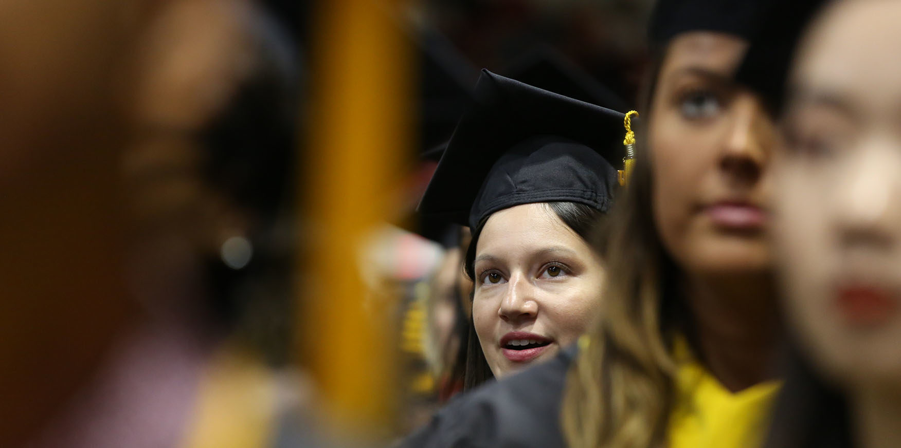 Female student peering through a group of other graduates at the 2019 CPS Graduation. Photo by Heratch Ekmekijan